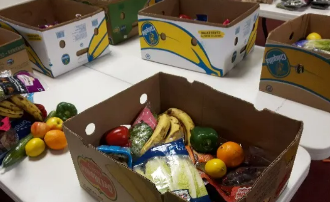 Des boites de cartons remplies de fruits et de légumes sur une table blanche.