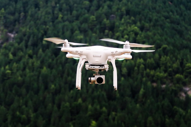 Un appareil volant blanc est au dessus d'une grande forêt. Il porte une caméra.