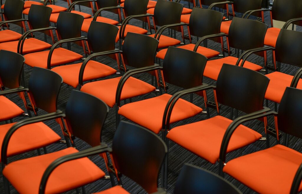 Des chaises au siège orange et au dossier noir sont placées en rangées.